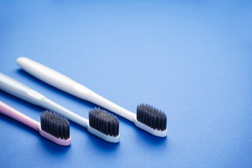 Multi-colored toothbrushes on a blue background with space for text, flat lay.