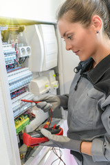 Woman electrician tests circuit breakers in a electrical panel