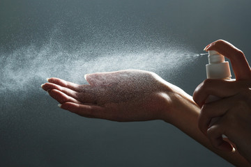Close-up view of human hand and antiseptic spray bottle on dark background. Sanitation of hands. Control Epidemic Prevention measures of coronavirus. - obrazy, fototapety, plakaty