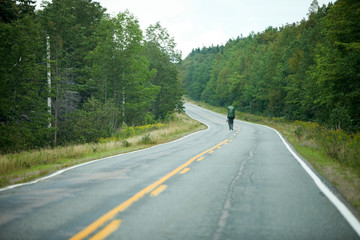 Fototapeta premium Backpaker idący środkiem drogi przez las.