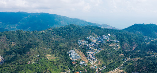 Aerial view of green mountain hills with built-up villas luxury for seasonal rent, housing surrounded by palm trees on an island in Samui, Thailand