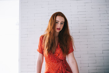 Peaceful relaxed red haired woman standing near white brick wall