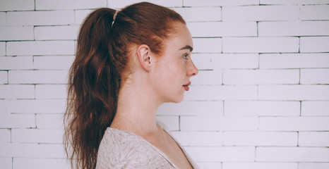Profile of adult female with long hair standing against brick wall in studio