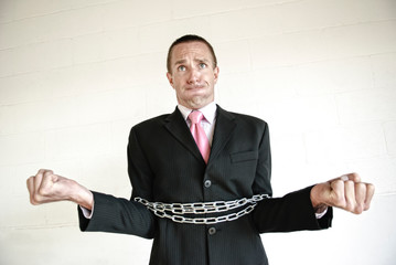 Businessman struggling against the loops of metal chain wrapped around the outside of his suit