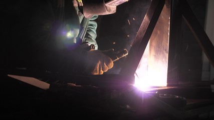 bright light and sparks from welding. Industrial worker in protective mask using a modern welding machine for welding metal structures in industrial production at a metal processing plant.