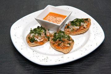 Chalupas con chicharrón de camarón, salsa picante, cilantro y cebolla, comida mexicana, plato blanco sobre fondo negro	