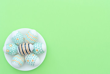 Decorated Easter egg lie on the white plate on green background. Happy Easter holiday concept. Greeting, invitation card. Flat lay style with copy space.