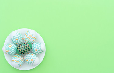 Decorated Easter egg lie on the white plate on green background. Happy Easter holiday concept. Greeting, invitation card. Flat lay style with copy space.