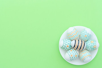 Decorated Easter egg lie on the white plate on green background. Happy Easter holiday concept. Greeting, invitation card. Flat lay style with copy space.