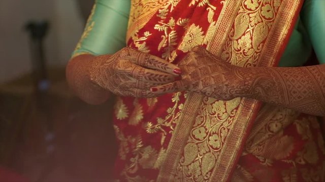 Indian woman is putting on the precious engagement ring with gemstone and tiny diamonds, dressed in traditional saree, with henna tattooed hands, partial front view