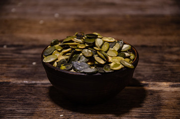 Peeled pumpkin seeds in a ceramic bowl on a wooden kitchen table.