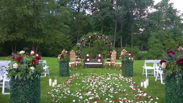 Chairs for wedding couple outdoor in the green garden and arch decorated with white and red peonies and petals on the grass, white chiavari chairs for the guests