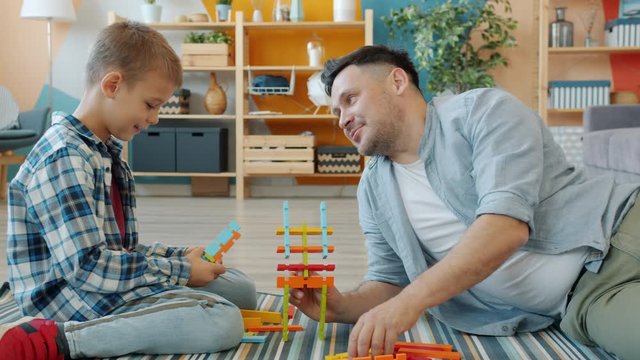 Adult man and little boy playing with wooden toys at home talking laughing enjoying game in free time. Communication and family activities concept.
