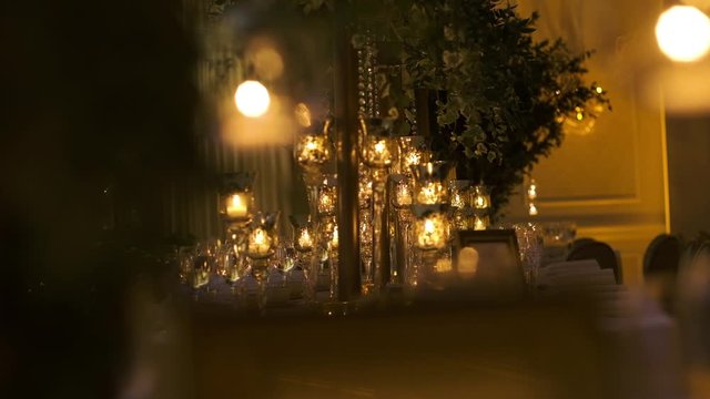 Rectangle table served with wine glasses, cutlery and glassware, decorated with stylish candlesticks, and green branches of eucalyptus and ruscus, front view