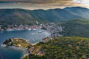 Aerial view of marina Vis at sunset, Croatia, a lot of chaotically standing boats in a bay, roofs of orange color, sunshine, hills with green trees, ferry station