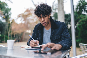 Pensive man browsing tablet and writing notes
