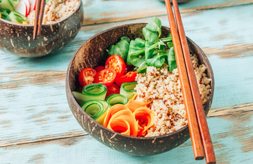 Vegan Buddha bowl. Healthy meal quinoa, tomato, cucumber, carrot, radish, corn salad in coconut bowls on blue rustic background.