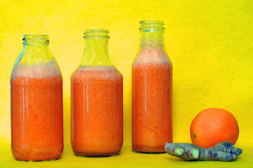 Glass bottles filled with colorful fresh homemade orange, carrot and ginger smoothies