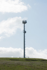 Fototapeta na wymiar Mobile phone cellular tower on grass with sky and clouds behind