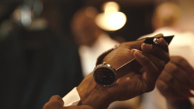 Man is dressing up for the important meeting, african man is holding watch and cufflink in the hand, groom is preparing for the wedding day