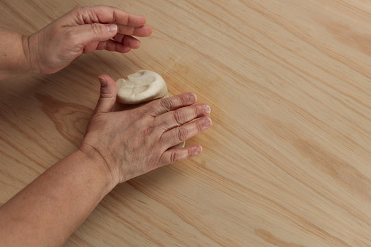 Overhead View Of The Hands Of An Adult Woman Kneading Pizza Dough In A Wooden Table In The Kitchen