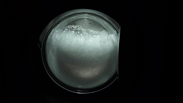 The problem is with an overdose or the wrong choice of detergent, a lot of foam. The washing machine on a black, dark background. Spinning drum. The washing process in the washing machine.