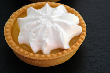 Tartlet with lemon cream and whipped squirrels. Round cake on a shortcrust pastry. Shortcrust tartlet and whipped cream on a black background.