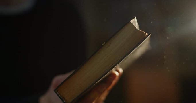 Close-up, hands are closes a very old book and dust fron it is fliying. Ray of light. 4K