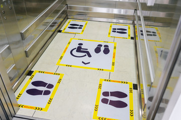 View of footprint sign for stand in lift. Social distancing with COVID-19 coronavirus crisis.yellow...