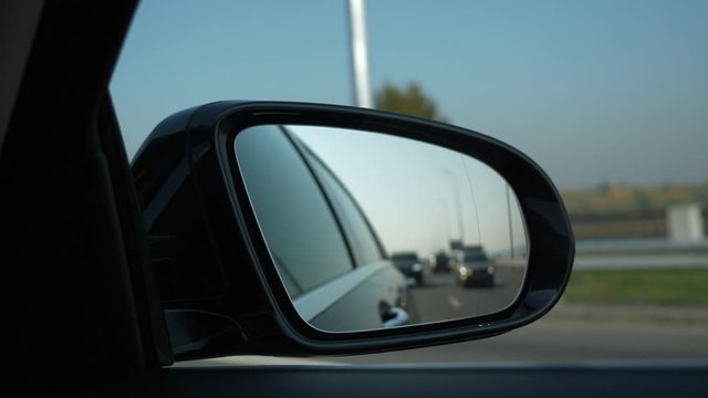 Close-up Side-view mirror Reflection Car Moving Behind Following on Highway. Bright Sunny Summer Autumn Morning Day, Blue Sky. 2x Slow motion 0.5 speed 60 FPS