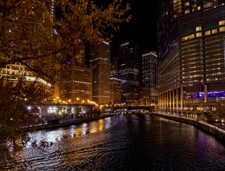 Night view of downtown Chicago lake in autumn with large sky scrapers and lights reflecting on water below.