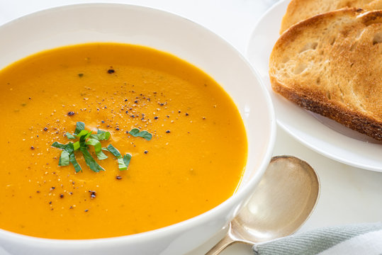 Homemade pumpkin soup in white bowl with bread on the side, close up view