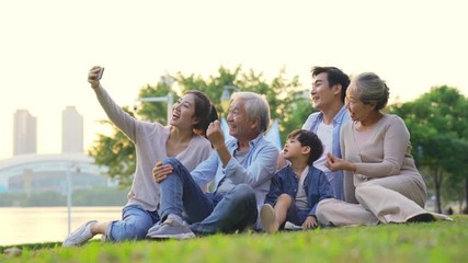 happy three generation asian family sitting on grass outdoors taking a selfie - Powered by Adobe