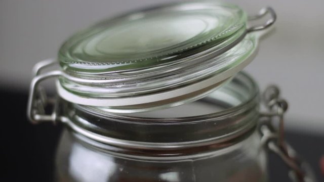 Close up of opening the clasp on a glass mason jar and lifting the lid before tilting the jar forwards