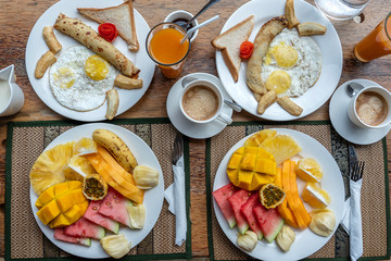 Tropical breakfast of fruit, coffee and scrambled eggs and banana pancake for two on the beach near sea