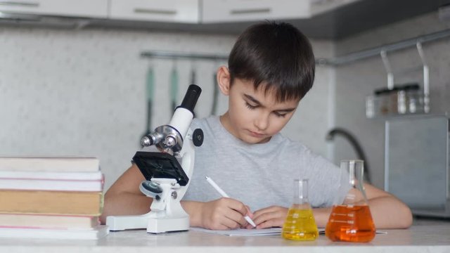 A boy learns chemistry using a microscope and makes notes in a notebook. Homework