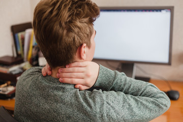Tired man after working at the computer massages rubs his neck, chronic pain in the neck and back,...