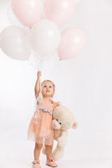 Little cute girl holds branch of balloons and large Teddy bear enjoy festive birthday event wear pink pastel summer dress isolated on a white background.
