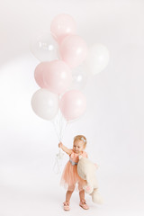 Little cute girl holds branch of balloons and large Teddy bear enjoy festive birthday event wear pink pastel summer dress isolated on a white background.