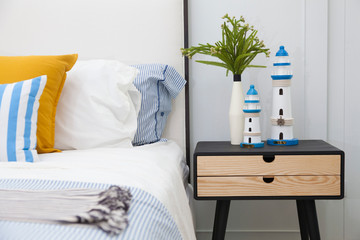 Bright bedroom interior with striped pillow on bed and bedside table lamp with plant vase on it.