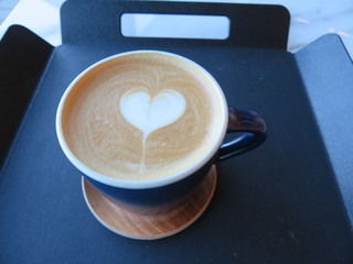 Hot latte with heart foam art, isolated on a dark brown serving tray