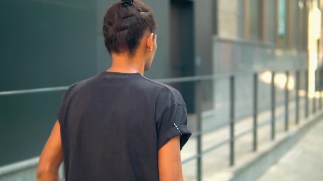 back view hipster guy walking along modern building person in casual t-shirt summer season in city slow motion
