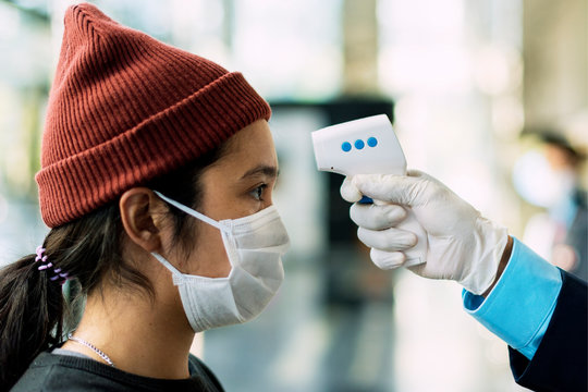 Woman in a medical mask getting her temperature measured by an electronic thermometer - Powered by Adobe