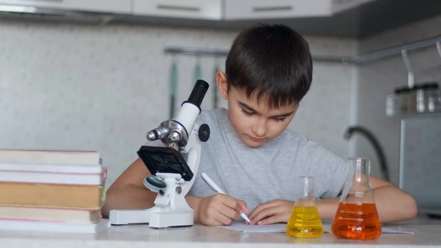 Close-up. A schoolboy teaches chemistry using a microscope and flasks with liquid and makes notes in a notebook. Homework.