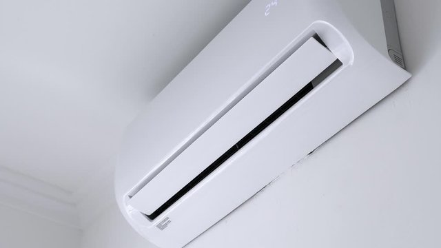 Flat air conditioner on white wall in room interior. Man pushing button on remote. Setting temperature