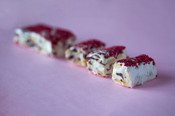 Torrone or nougat bar with nuts and red dried berries. Traditional italian dessert close up on pink background. Sweet tasty and healthy food