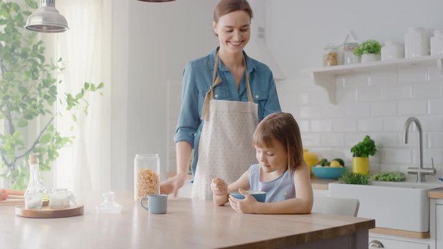 Breakfast in the Kitchen: Young Beautiful Mother Pours Cereal into Bowl, Adorable Little Daughter Starts Eating with Pleasure. Caring Mother Prepares Cereal Breakfast for Her Cute Little Girl