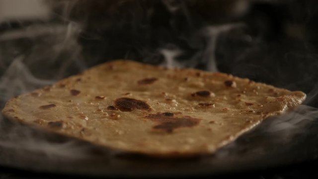 Close up of steaming hot roti cooked on a cast iron pan and flipping with bare hands