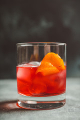 Red traditional old fashioned cocktail with orange zest on the rustic background. Selective focus. Shallow depth of field.