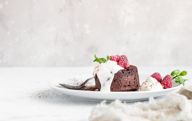 Delicious chocolate fondant or lava cake with cream, raspberries and cream, light grey concrete...